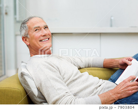 Senior man sitting on sofa reading book 7903804