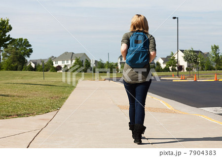 Female high school student walking along pavement 7904383
