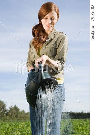 Young woman watering plants in field Young woman watering plants in field 7905082