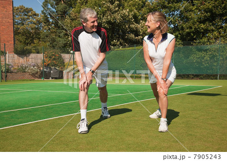Mature woman and senior man performing warming up exercises on tennis court 7905243