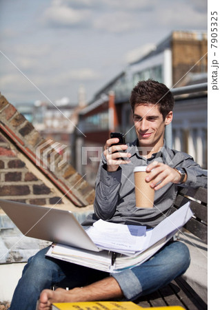 Young man sitting in a roof garden with laptop and mobile phone 7905325