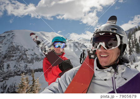 Young woman and mid adult man in skiwear carrying skis on shoulder, smiling 7905679