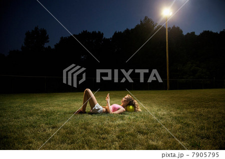 Girl using cell phone lying on soccer pitch at night Girl using cell phone lying on soccer pitch at night 7905795