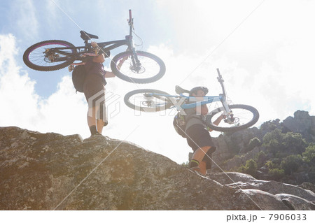 Young couple carrying mountain bikes down rocks 7906033