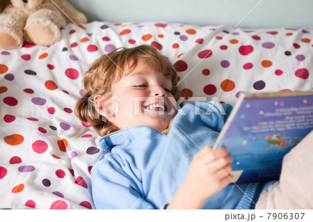 Young boy reading a book on his bed 7906307