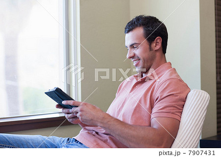 Young man using electronic book, smiling 7907431