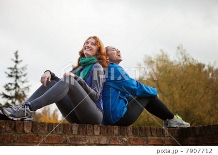 Young women sitting back to back on brick wall Young women sitting back to back on brick wall 7907712