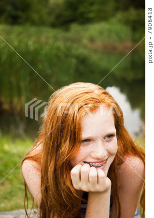 Teenage girl smiling at friends with a lake behind her Teenage girl smiling at friends with a lake behind her 7908418