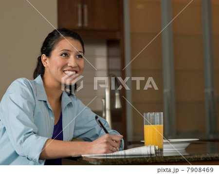 Young woman reading newspaper over orange juice, smiling 7908469