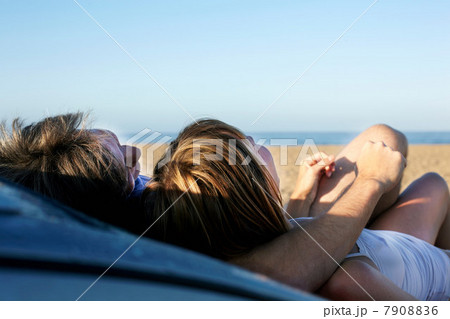 Mid adult couple relaxing on car on beach 7908836