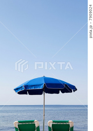 Blue parasol and sun loungers by the sea 7909024