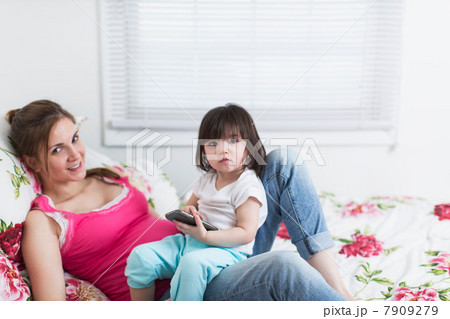 Portrait of pregnant woman and toddler daughter lounging on bed with smartphone Portrait of pregnant woman and toddler daughter lounging on bed with smartphone 7909279