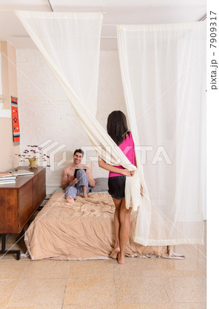 Young man using digital tablet in bed, woman by curtain 7909317