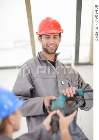 Male and female laborer handing electric drill on construction site 7909409
