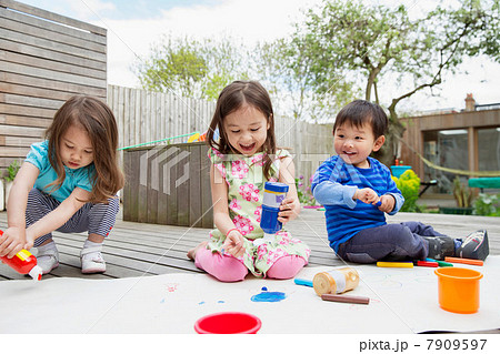 Three young children painting and drawing in garden 7909597