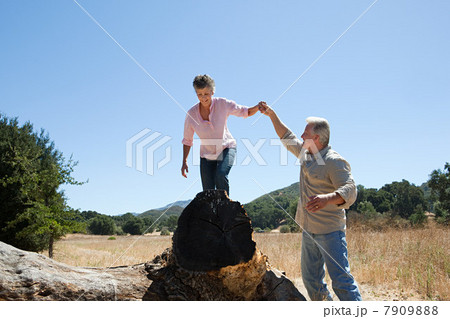 Man holding woman's hand as she walks over log 7909888