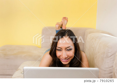 Mid adult female lying on sofa looking at laptop 7910265