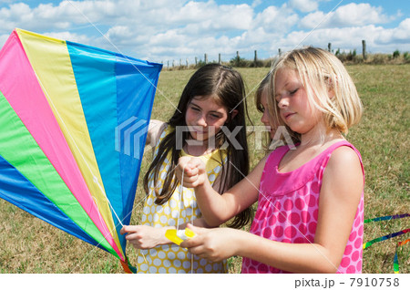 Three girls holding kite in field 7910758