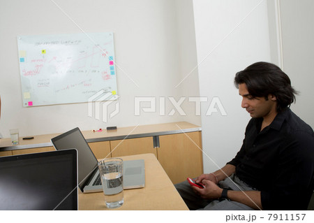 Young man at desk with cell phone Young man at desk with cell phone 7911157