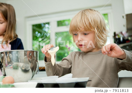 Boy spooning cake mixture into cake cases 7911813