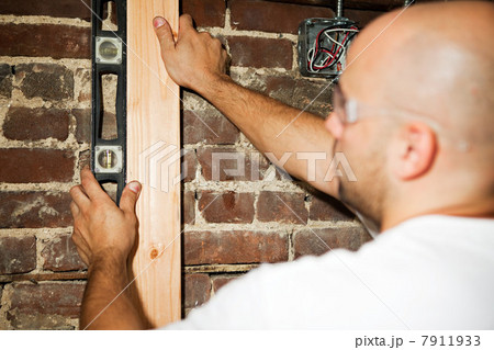 Man using spirit level against brick wall 7911933