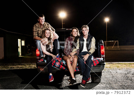 Portrait of friends sitting on tailgate of car at night 7912372