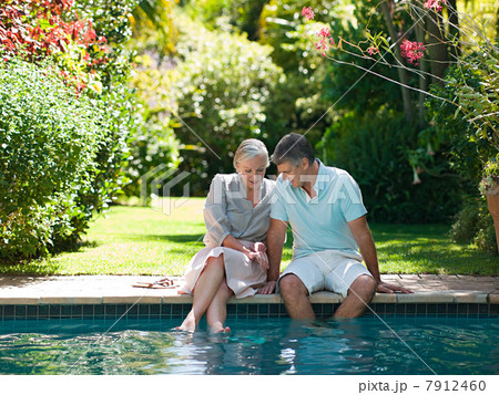 Couple sitting at poolside in garden Couple sitting at poolside in garden 7912460
