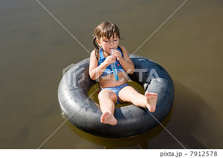 Girl eating lolly on inflatable ring in lake 7912578