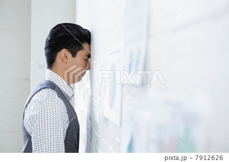 Young man in office with head against wall 7912626