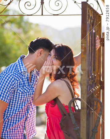 Young woman whispering to man by iron gate, portrait Young woman whispering to man by iron gate, portrait 7912658