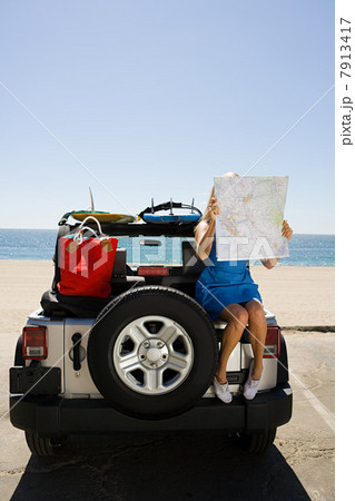 Young woman sitting on vehicle looking at map Young woman sitting on vehicle looking at map 7913417