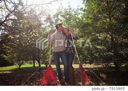 Affectionate couple with leaf rakes Affectionate couple with leaf rakes 7913903