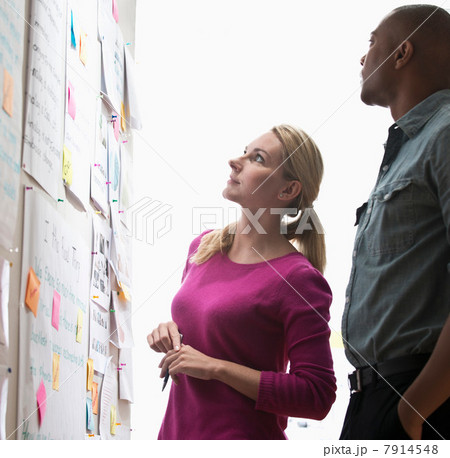 Colleagues looking at adhesive notes and paper on wall Colleagues looking at adhesive notes and paper on wall 7914548