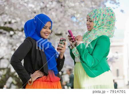 Two young females in park looking at their mobile phones Two young females in park looking at their mobile phones 7914701