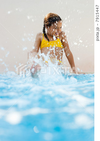 Girl sitting at poolside kicking and splashing 7915447
