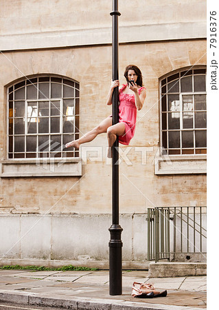 Woman in pink dress using cellphone on street lamp in city 7916376