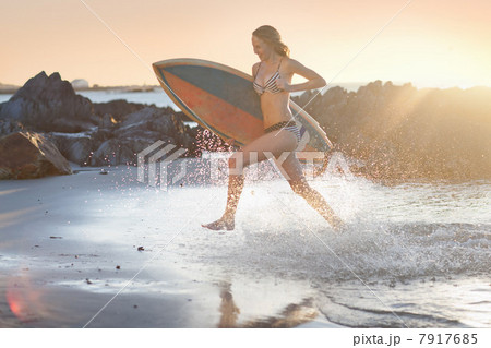 Young woman with surfboard running on beach 7917685