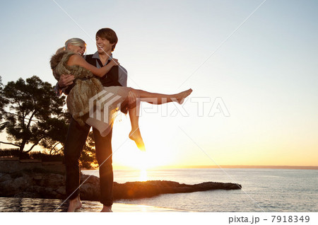 Man carrying girlfriend by the ocean at sunset 7918349