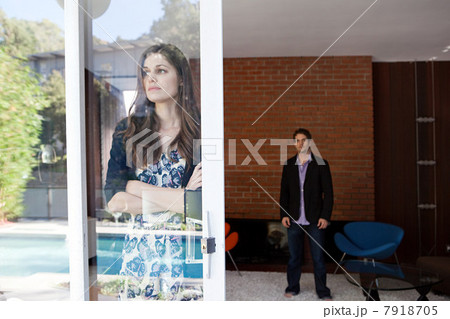 Woman looking through window with arms crossed, man in background 7918705