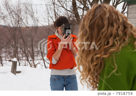 Teenage girl taking photograph of friend in snow 7918759