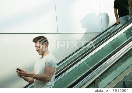 Young man on escalator using smartphone 7919004