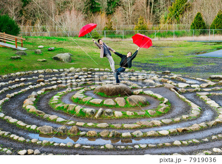 Mid adult dancers performing with red umbrellas in stone circle 7919036