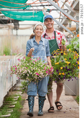 Young woman and mature man walking with hanging baskets in garden centre 7919157
