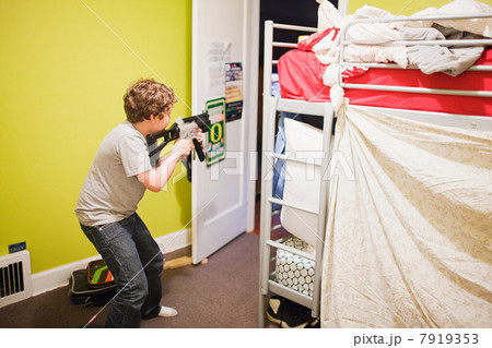 Boy playing with toy gun in bedroom 7919353