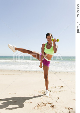 Woman standing on one leg with hand weight on beach 7919459