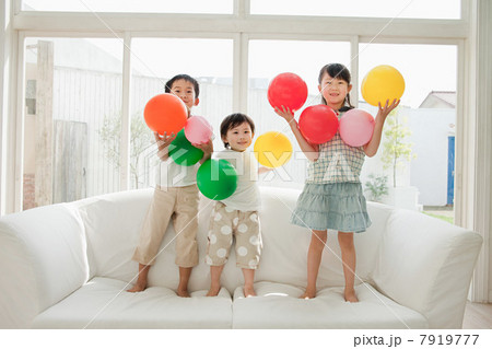 Three children standing on sofa with balloons 7919777