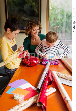 Woman and sons wrapping gifts at table 7920386