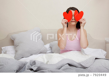 Woman in bed holding heart shapes over eyes Woman in bed holding heart shapes over eyes 7920449