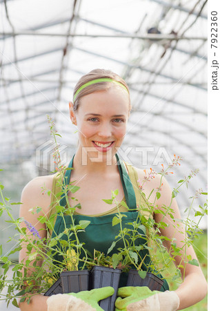 Mid adult woman holding plants in garden centre, portrait Mid adult woman holding plants in garden centre, portrait 7922360