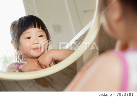 Toddler looking in mirror whilst fastening her dress 7923381
